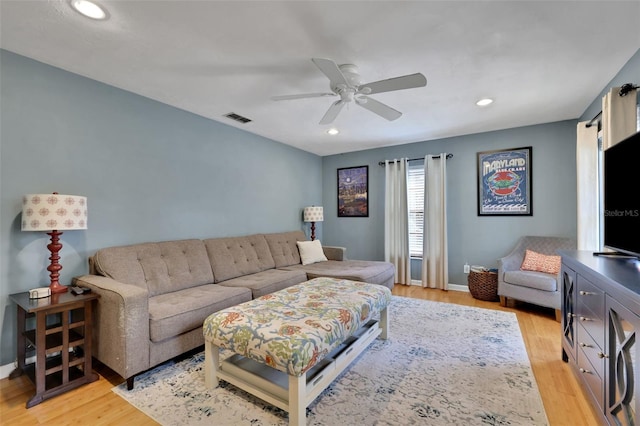 living room featuring light wood-style floors, ceiling fan, visible vents, and baseboards