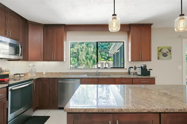 kitchen with light stone counters, stainless steel appliances, a sink, and pendant lighting