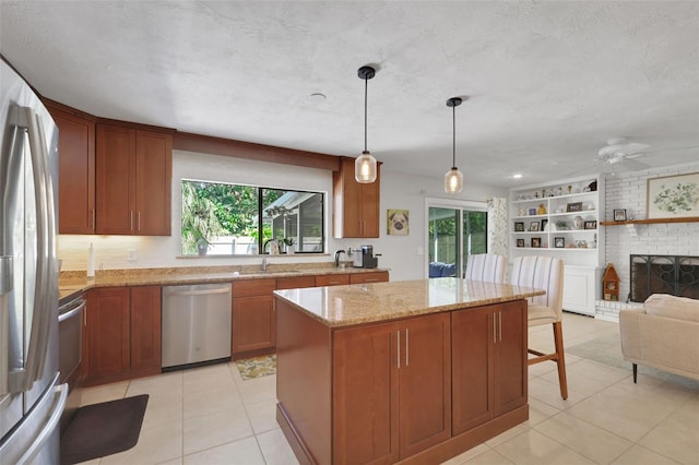 kitchen with a center island, light stone countertops, stainless steel appliances, a brick fireplace, and a sink