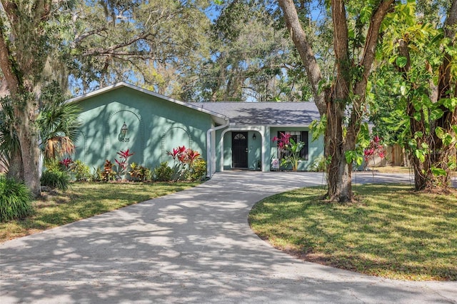 ranch-style home with a front yard, driveway, and stucco siding