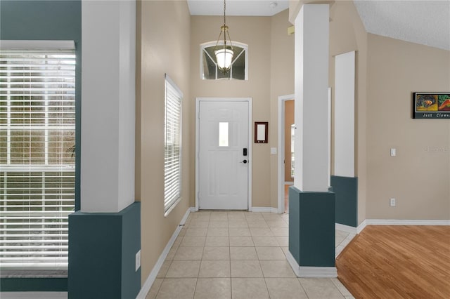 entryway with high vaulted ceiling, decorative columns, baseboards, and light tile patterned floors