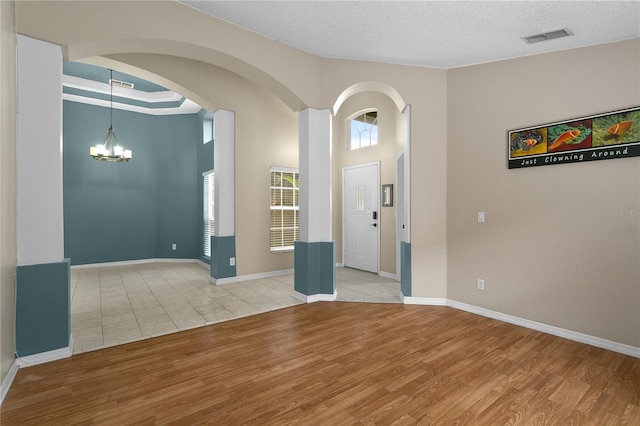 foyer with arched walkways, wood finished floors, visible vents, and an inviting chandelier