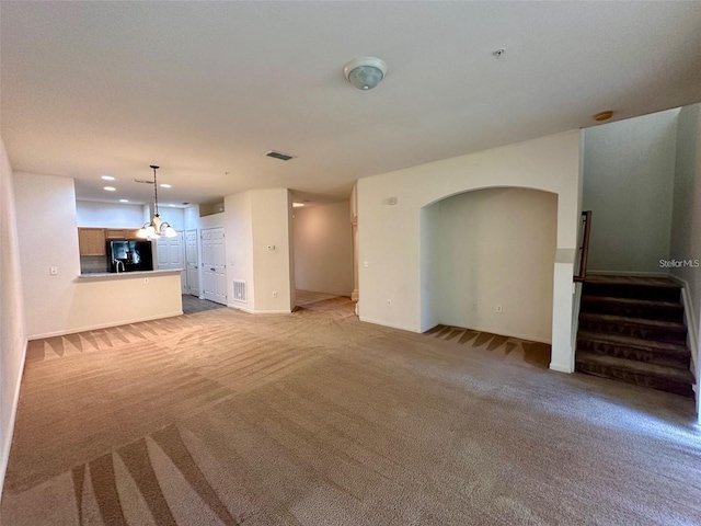 unfurnished living room featuring arched walkways, recessed lighting, light colored carpet, visible vents, and stairway