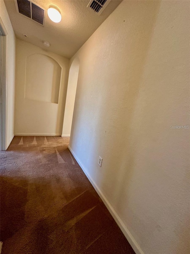 hall featuring baseboards, visible vents, a textured ceiling, and carpet flooring