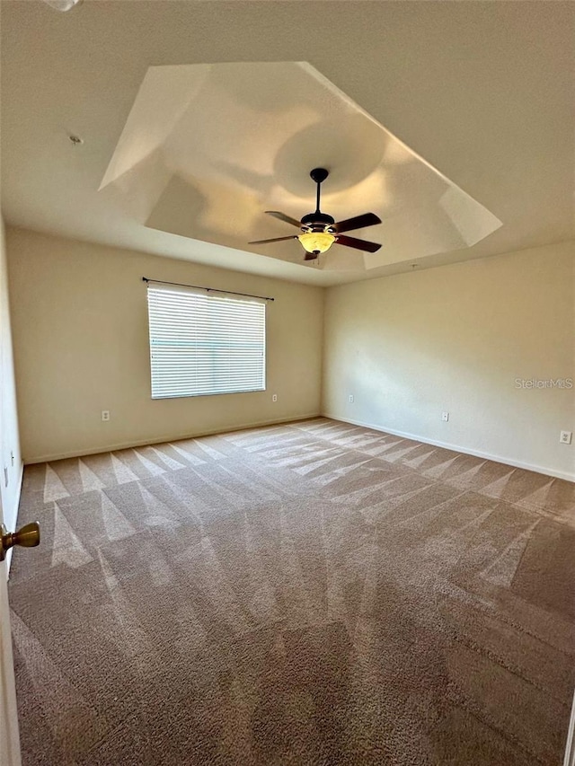 carpeted empty room with a tray ceiling, ceiling fan, and baseboards