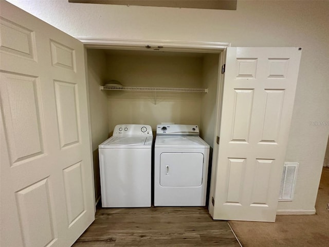 clothes washing area featuring washing machine and dryer, laundry area, visible vents, and wood finished floors