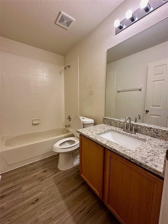 bathroom with a textured ceiling, toilet, wood finished floors, visible vents, and tub / shower combination