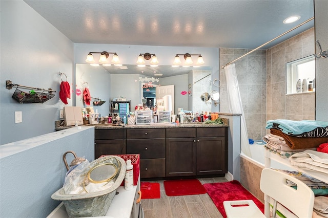 bathroom featuring a textured ceiling, tiled shower / bath, vanity, and wood finished floors