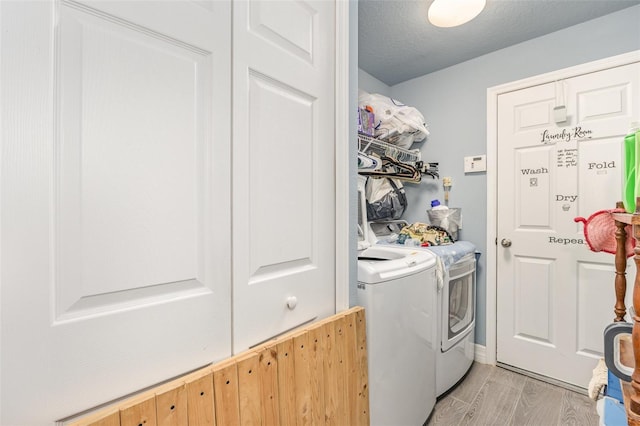 clothes washing area featuring light wood-style floors, laundry area, a textured ceiling, and washing machine and clothes dryer