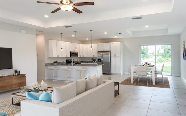 living room featuring light tile patterned flooring, recessed lighting, a ceiling fan, baseboards, and a tray ceiling