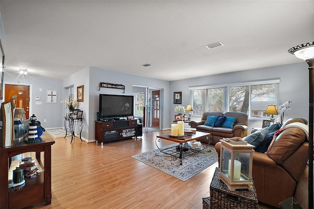 living area with light wood finished floors, visible vents, and baseboards