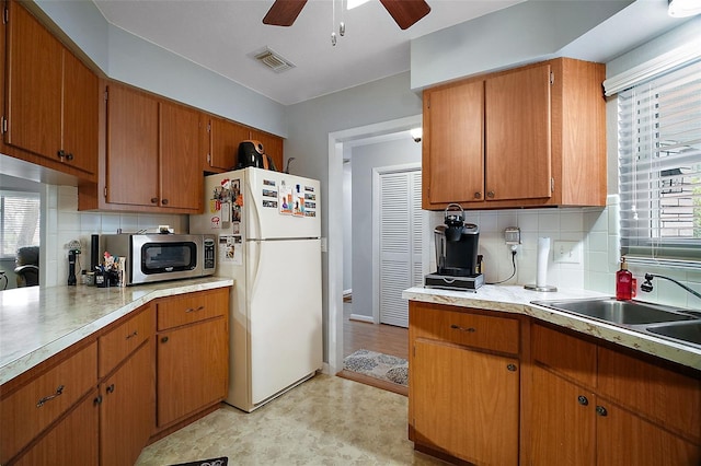 kitchen with stainless steel microwave, brown cabinets, freestanding refrigerator, light countertops, and a sink