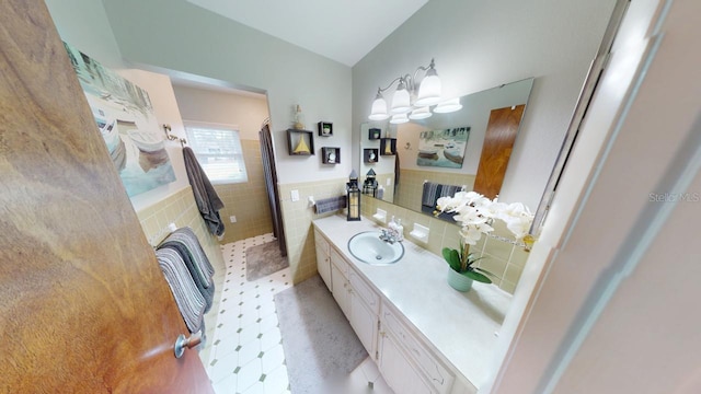 bathroom with a wainscoted wall, vanity, tile walls, vaulted ceiling, and a tile shower