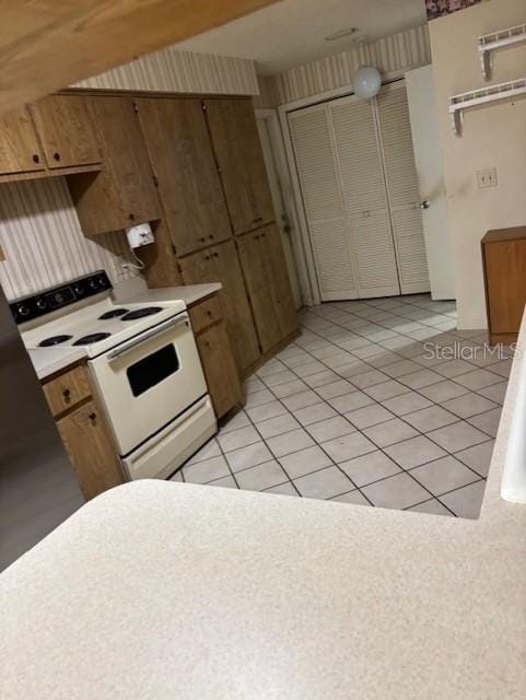 kitchen featuring brown cabinets, light tile patterned floors, white electric stove, and light countertops