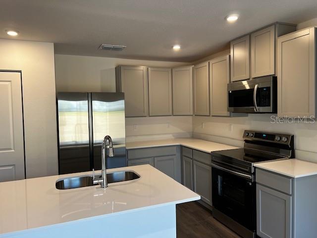 kitchen featuring a center island with sink, visible vents, appliances with stainless steel finishes, gray cabinets, and light countertops