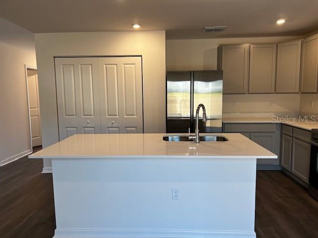 kitchen featuring a kitchen island with sink, a sink, visible vents, light countertops, and fridge