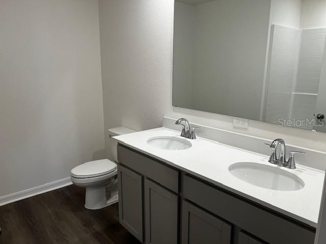 full bath with toilet, double vanity, a sink, and wood finished floors