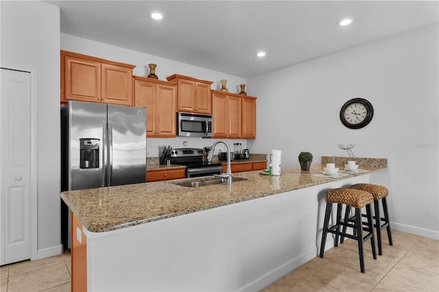 kitchen with stainless steel appliances, brown cabinetry, a kitchen bar, and light stone countertops