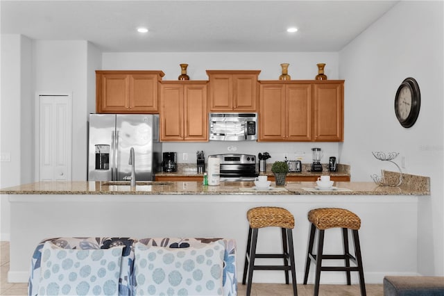 kitchen with brown cabinets, stainless steel appliances, recessed lighting, a sink, and light stone countertops