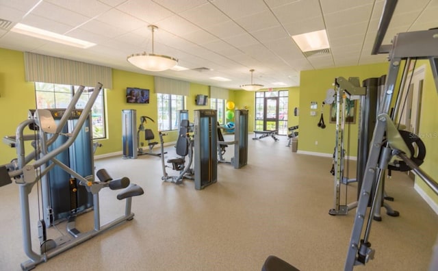 exercise room with a paneled ceiling, visible vents, baseboards, and a wealth of natural light