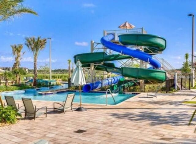 pool featuring a water slide, a water play area, and a patio