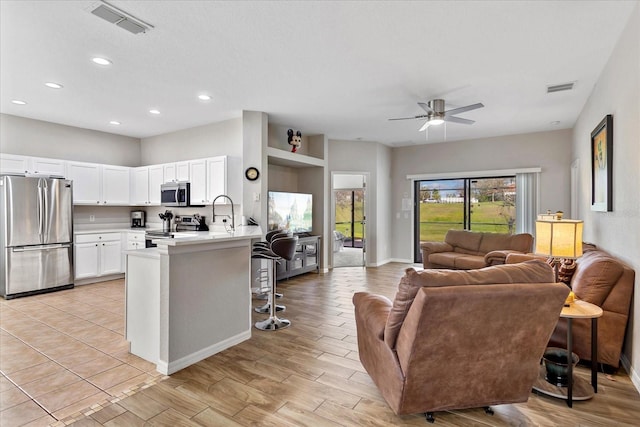 kitchen with open floor plan, a peninsula, stainless steel appliances, light countertops, and white cabinetry