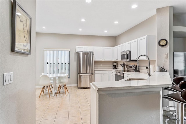 kitchen featuring appliances with stainless steel finishes, a breakfast bar, a peninsula, light countertops, and a sink