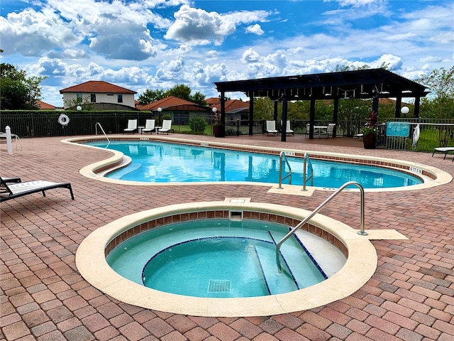 community pool with a patio area, fence, and a hot tub