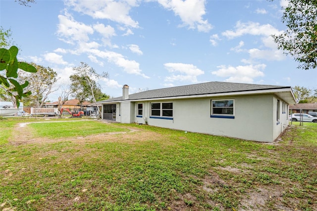 back of property featuring a lawn, a chimney, and stucco siding