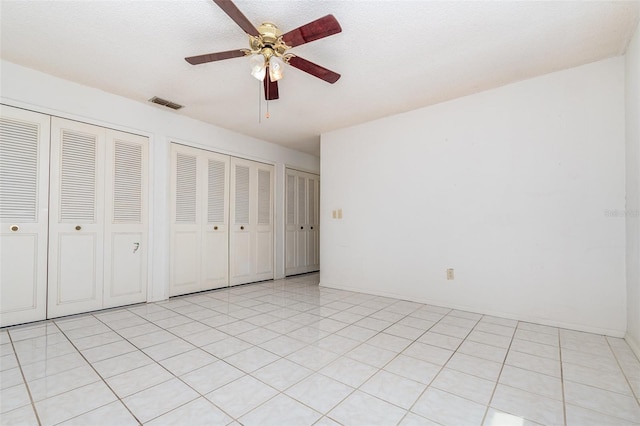 unfurnished bedroom featuring multiple closets, visible vents, ceiling fan, a textured ceiling, and baseboards