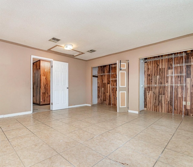 tiled empty room featuring baseboards, visible vents, ornamental molding, and a textured ceiling