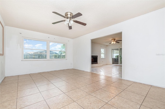 unfurnished room with a large fireplace, light tile patterned floors, a ceiling fan, and a textured ceiling