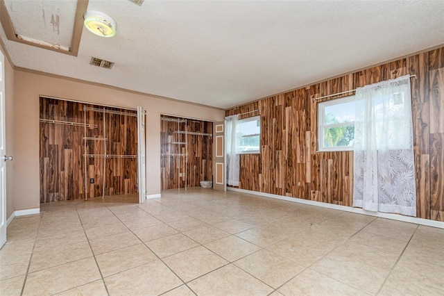 tiled spare room featuring wood walls, baseboards, visible vents, and a textured ceiling