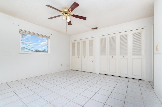 unfurnished bedroom with multiple closets, visible vents, ceiling fan, and a textured ceiling