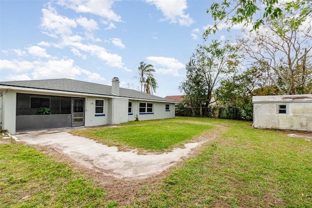 back of property featuring an outbuilding, fence, a sunroom, driveway, and a lawn