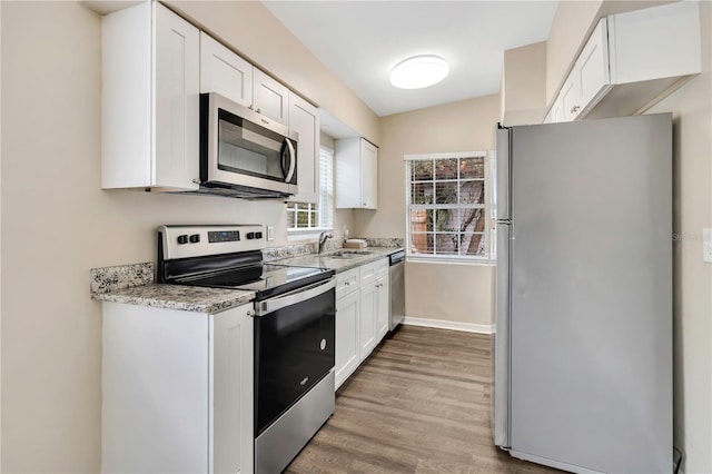 kitchen featuring light wood finished floors, appliances with stainless steel finishes, white cabinets, a sink, and baseboards