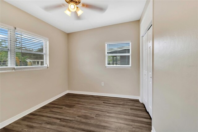 unfurnished bedroom featuring a closet, dark wood-style flooring, multiple windows, and baseboards