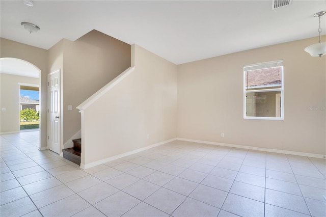 empty room featuring light tile patterned floors, visible vents, arched walkways, baseboards, and stairway