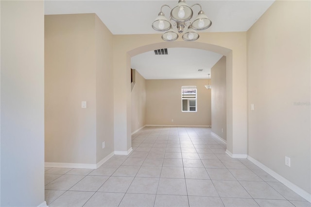 empty room featuring arched walkways, a notable chandelier, visible vents, light tile patterned flooring, and baseboards