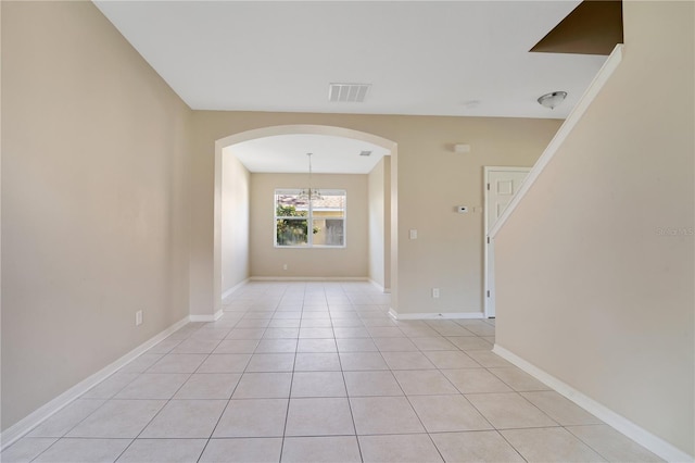 empty room with arched walkways, visible vents, baseboards, and light tile patterned floors