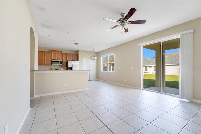 unfurnished living room featuring arched walkways, light tile patterned flooring, ceiling fan with notable chandelier, visible vents, and baseboards