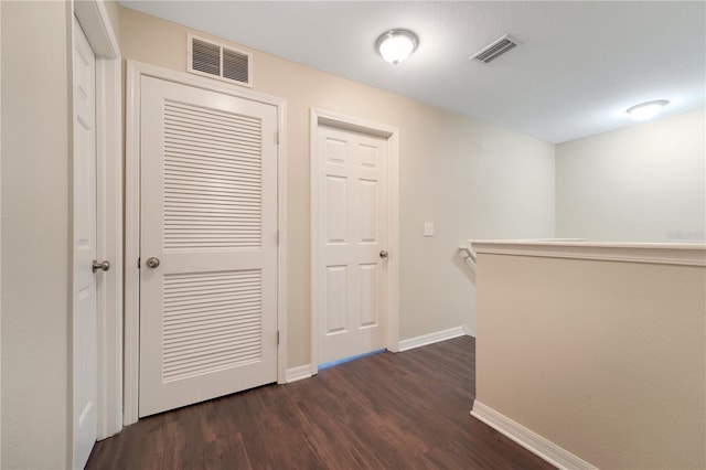 corridor featuring dark wood-style floors, baseboards, visible vents, and an upstairs landing