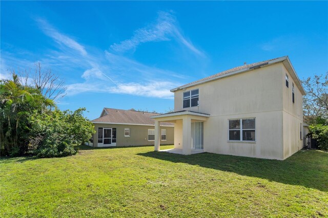 rear view of house featuring stucco siding, a patio, and a yard