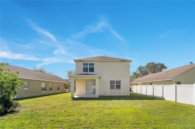 back of property with stucco siding, fence, and a yard