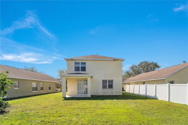 rear view of house featuring a yard, fence, and stucco siding