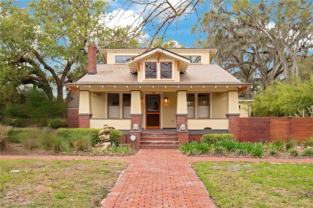 bungalow-style house featuring a porch, a chimney, brick siding, and stucco siding