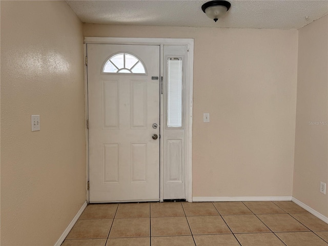 foyer entrance with a textured ceiling, baseboards, and light tile patterned floors