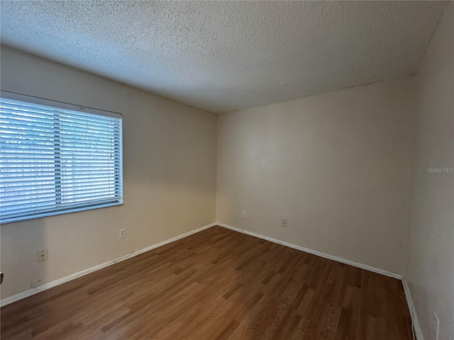 spare room featuring dark wood-style floors, a textured ceiling, and baseboards