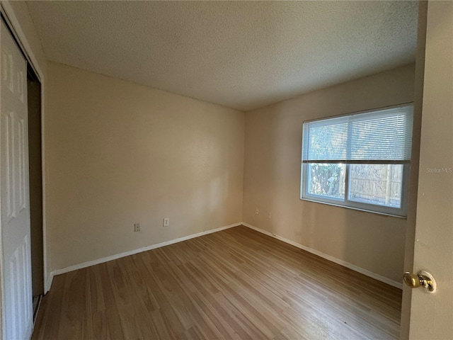 spare room with light wood finished floors, baseboards, and a textured ceiling