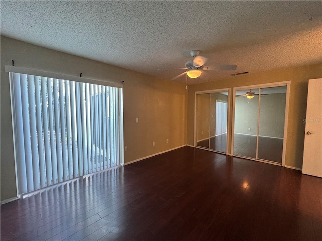 unfurnished bedroom with a textured ceiling, dark wood finished floors, visible vents, and multiple closets